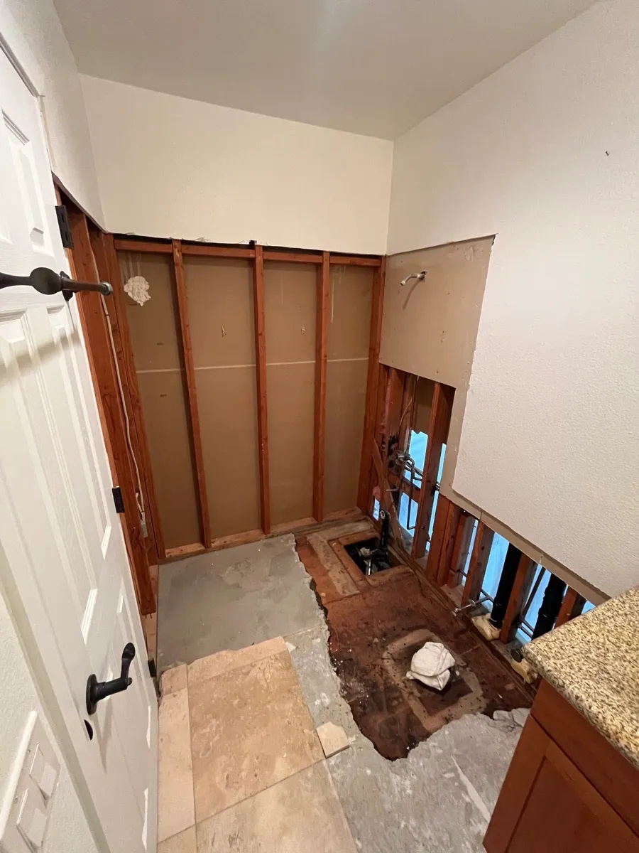 AWC bathroom with lower wall finishes removed, exposing framing, piping and subfloor.